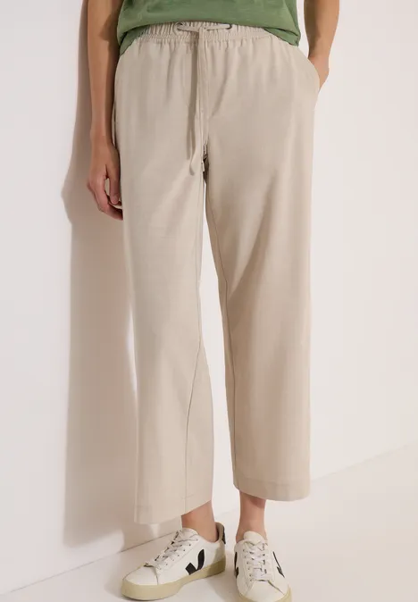 Pantalon large beige mi-longue aux chevilles, fluide et porté avec des baskets claires.