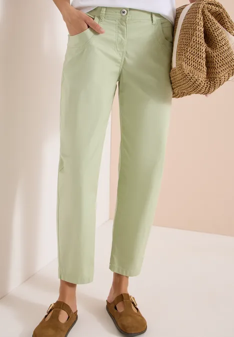 Barrel Leg Hose in Papertouch Qualität raw matcha lime Model trägt hellgrüne, knöchellange Hosen, braune Wildleder-Mules und hält einen geflochtenen Korb.