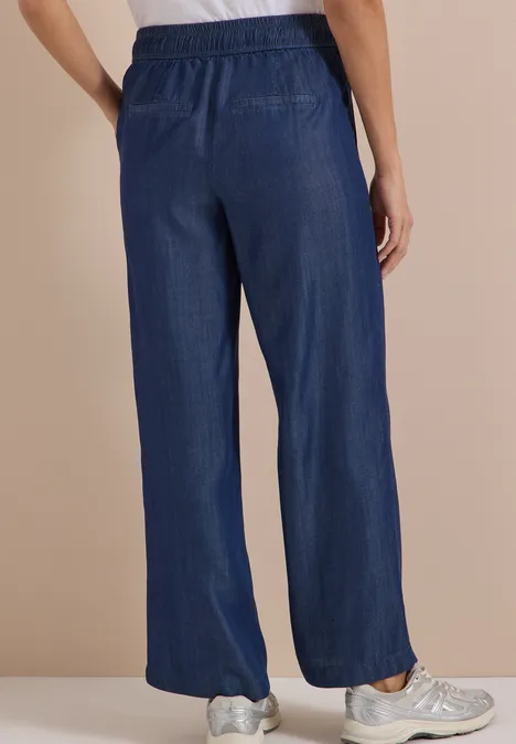 Person von hinten in weiten, marineblauen Hosen und Sneakern.