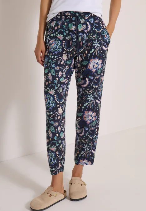Hose mit blau-grünem Blumenmuster, lockere Passform, kombiniert mit hellen Slippern.