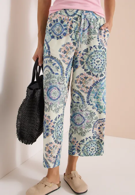 High Waist Wide Leg Hose im Loose Fit vanilla white Weite Sommerhose mit blau-grünem Ornamentprint, kombiniert mit rosa Top, schwarzer Tasche und Slippern.