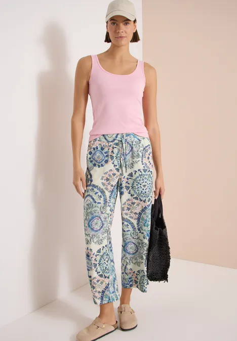 High Waist Wide Leg Hose im Loose Fit vanilla white Frau trägt rosa Top, gemusterte blaue Hose, beigefarbene Schuhe und schwarze Tasche.