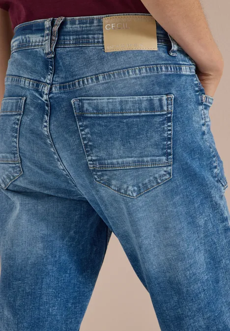 Rückansicht einer Person in locker sitzenden blauen Jeans mit zwei Gesäßstaschen und sichtbarem Label am Bund.