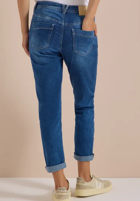 Person von hinten mit hochgekrempelten blauen Jeans und cremefarbenen Sneakern.