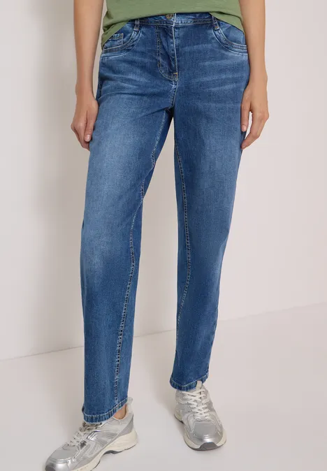 Eine Person trägt blaue Jeans und silberne Sneaker vor neutralem Hintergrund.