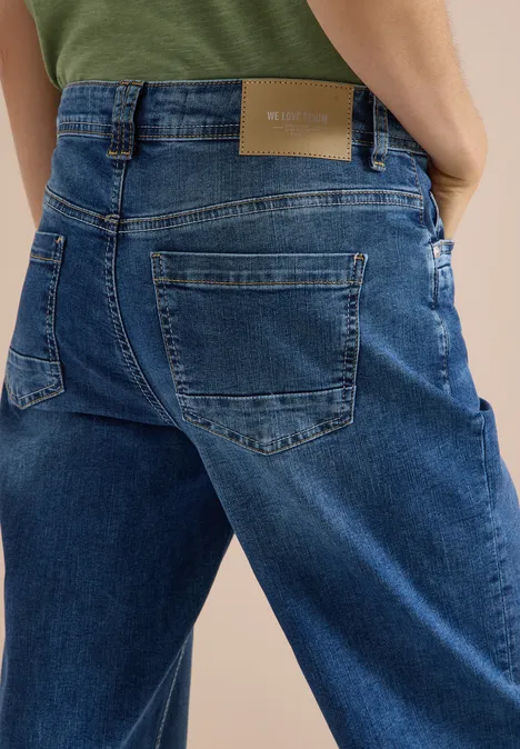 Rückenansicht einer Person in lockeren blauen Jeans und grünem Oberteil, Nahaufnahme