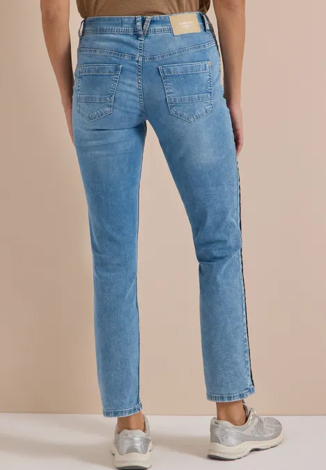 Hinteransicht einer Person in hellblauen Jeans und Sneakers vor beigem Hintergrund.