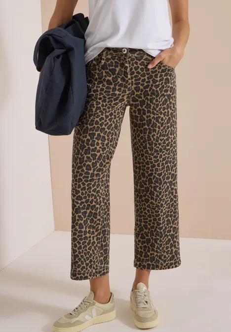 High Waist Wide Leg Jeans mit Leo-Muster creamy mocha Eine Person trägt eine weiße Bluse, weite Leo-Hose und Sneaker vor beigem Hintergrund.