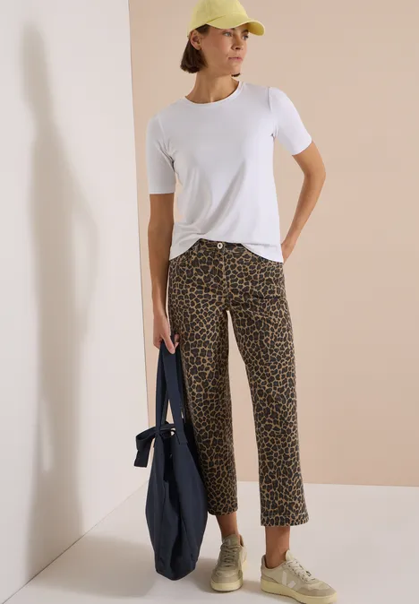 High Waist Wide Leg Jeans mit Leo-Muster creamy mocha Dame in weißem T-Shirt, legeren Leo-Hose, gelber Cap, grünen Sneakers und großer blauer Tasche.