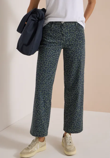 Weite, gemusterte Hose mit grünem Print, kombiniert mit weißen Sneakern, weißem T-Shirt und blauer Umhängetasche.