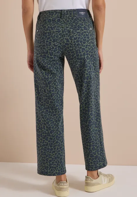 Person steht mit dem Rücken zur Kamera, trägt weite Hose mit blau-grünem Leopardenmuster und weiße Sneaker.