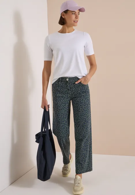 Frau trägt weißes T-Shirt, locker sitzende gemusterte Hose, Cap, hält große Stofftasche.