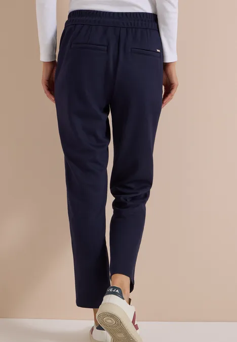 Vue arrière d'une personne en pantalon de jogging bleu marine et baskets sur fond beige.