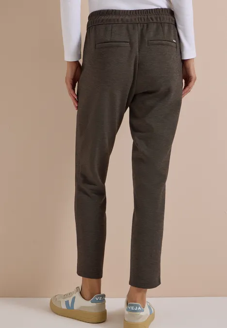 Vue arrière d'une personne portant un pantalon olive ajusté à taille élastique et des baskets claires.