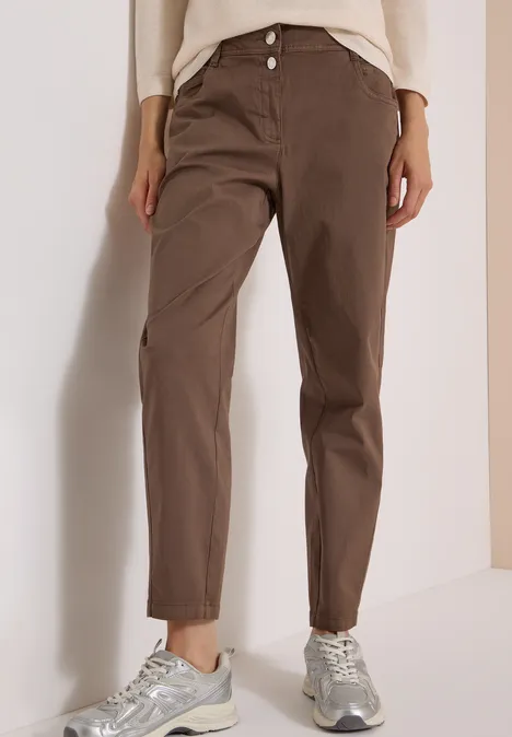 Mid Waist Barrel Leg Hose im Casual Fit urban taupe Een persoon draagt een losse bruine chino met hoge taille en zilverkleurige sneakers tegen een lichte achtergrond.
