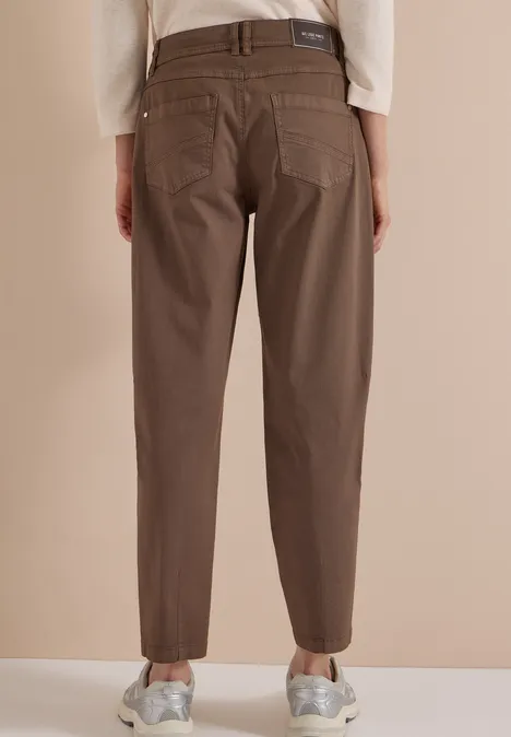 Mid Waist Barrel Leg Hose im Casual Fit urban taupe Achteraanzicht van een persoon met kastanjebruine broek en zilverkleurige sneakers voor een beige achtergrond.