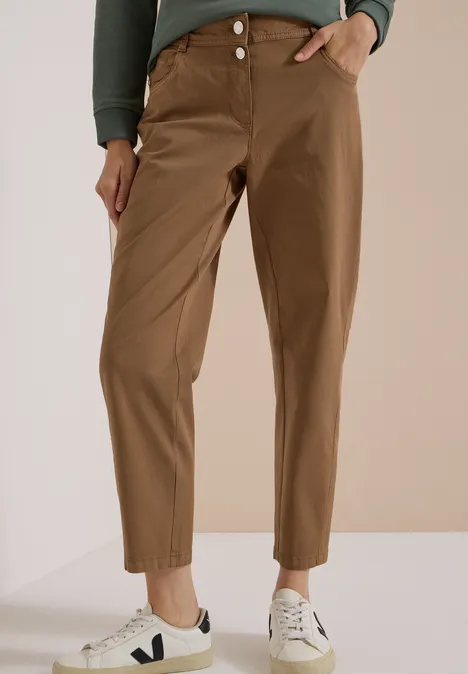 Personne porte un pantalon marron taille haute, plis devant jusqu'aux chevilles et des baskets blanches.