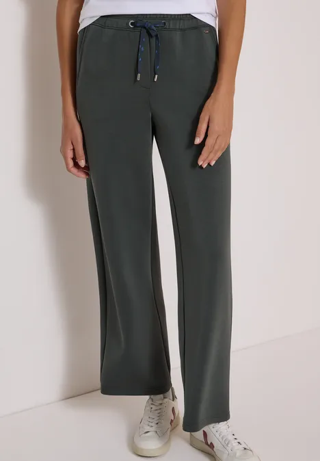 Spodnie z szerokimi nogawkami z tkaniny o fakturze przypominającej Silk Touch faded olive Szare szerokie spodnie ze ściągaczem w pasie, zestawione z białymi trampkami.