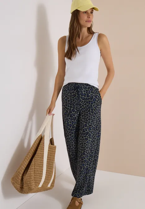Broek met Wide Leg pijpen van Silk-Touch-kwaliteit dried olive green Frau im weißen Top, weiten Leo-Hose, gelber Cap und geflochtener Einkaufstasche.
