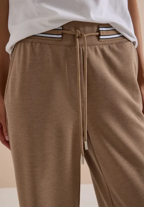 Person trägt beige Jogginghose mit Tunnelzug und Streifen an der Taille.