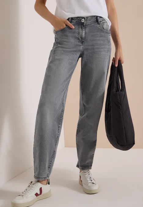 High Waist Barrel Leg Jeans w stylu Loose Fit light grey wash Kobieta ma na sobie szare dżinsy, białe trampki i trzyma czarną torbę.