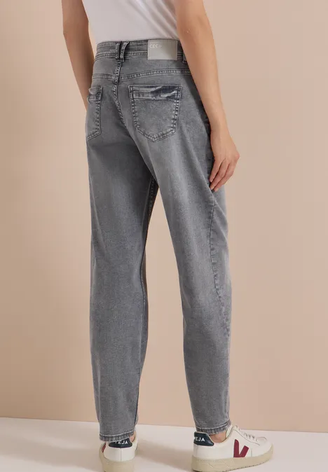 High Waist Barrel Leg Jeans w stylu Loose Fit light grey wash Kobieta w jasnoszarych dżinsach i białych trampkach, widok od tyłu na beżowym tle.