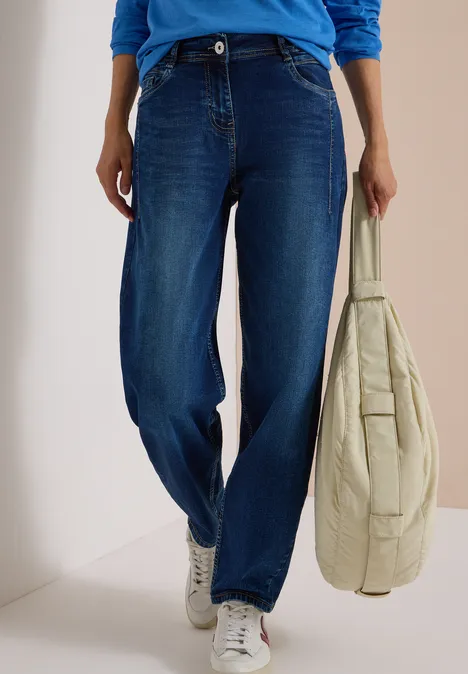 Jeans met High Waist en wijd uitlopende pijpen in een Loose Fit-pasvorm mid blue used wash Een persoon draagt een blauwe spijkerbroek, witte sneakers en houdt een lichte, doorgestikte tas vast.