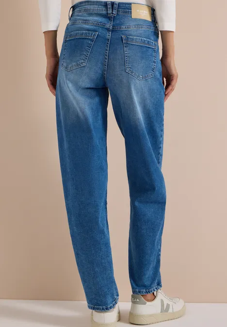 Jeans met High Waist en wijd uitlopende pijpen in een Loose Fit-pasvorm authentic used wash Rugaanzicht van een persoon met losse blauwe jeans en witte sneakers voor een beige achtergrond.