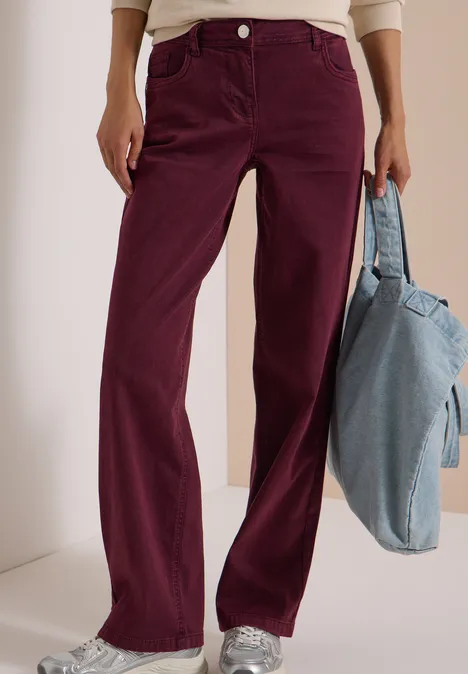 Weite bordeauxrote Cordhose, weißes Oberteil, silberne Sneaker und eine hellblaue Jeans-Tasche.