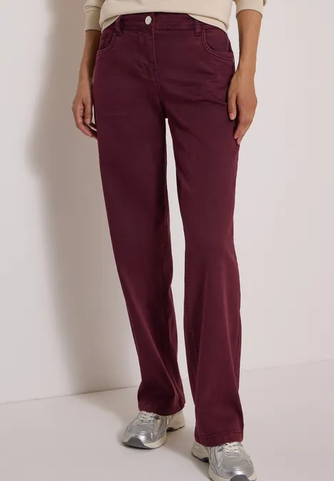 Eine Person trägt hoch taillierte, gerade geschnittene, bordeauxrote Jeans und silberne Sneaker.