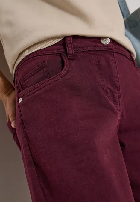 Nahaufnahme einer Person mit burgunderroter Hose und beigem Oberteil.