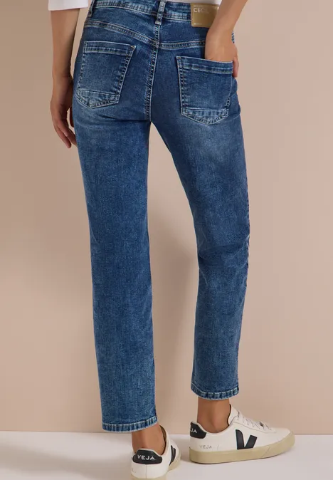 Frau in hoch taillierter, gerader Jeans und weißen Sneakern vor beigem Hintergrund.