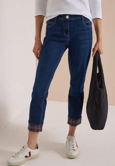 Person trägt dunkelblaue Jeans mit umgekrempelten Säumen, weiße Sneaker und schwarze Tasche.