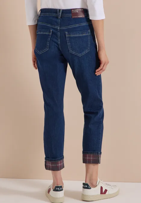 Rückansicht einer Person in dunkelblauen Jeans mit karierten Umschlagbündchen und weißen Sneakers.