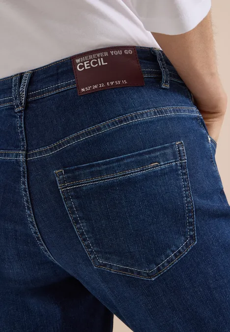 Rückenansicht einer Person in blauen Denim-Jeans mit aufgesetzter Gesäßtasche und Markenlabel am Bund.