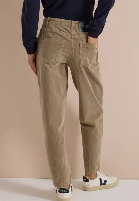 Mid Waist Barrel Leg Hose im Casual Fit creamy mocha Person von hinten in hellbeigen Cordhose und weißen Sneakern vor neutralem Hintergrund.
