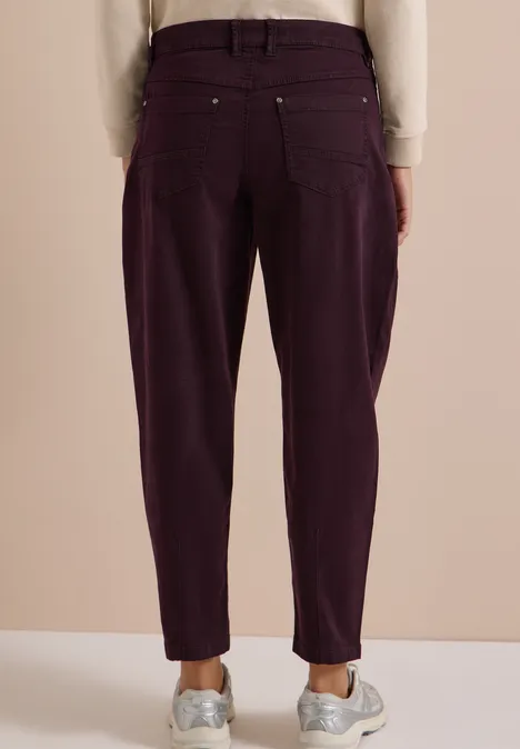Achteraanzicht van iemand in donkerpaarse high-waist broek en witte sneakers.