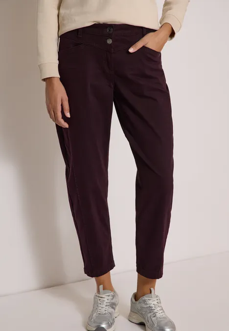 Damesbroek in donker aubergine met omgeslagen pijpen, gecombineerd met grijze sneakers en lichte trui.