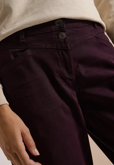 Close-up van paarse broek met knopen en een beige top, hand zichtbaar langs de heup.