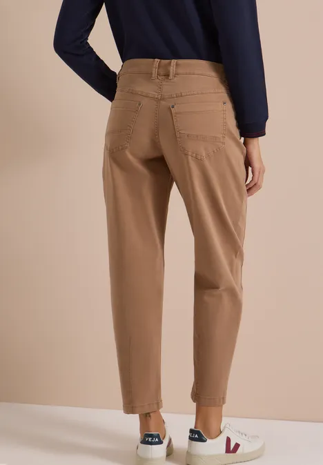 Vrouw van achter gezien in beige chino met omslag, donkerblauw shirt en witte sneakers.