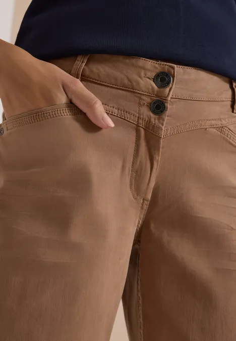 Bruine broek met twee knopen, hand in het zijvak gestoken.