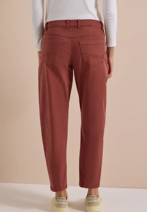 Achteraanzicht van een persoon in een bordeauxrode, losse broek met zakken tegen een neutrale achtergrond.