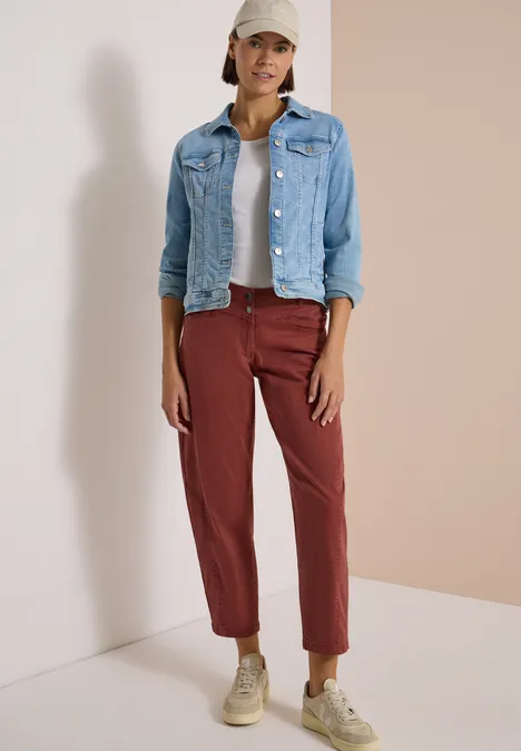 Vrouw met spijkerjasje, wit topje, bordeaux broek en pet voor neutrale achtergrond
