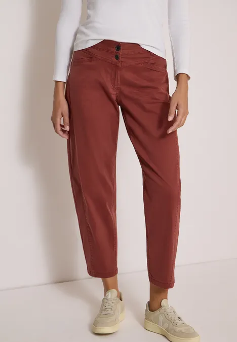 Onderlichaam in een wit shirt, bruinrode chino met opgeslagen pijpen en beige sneakers.
