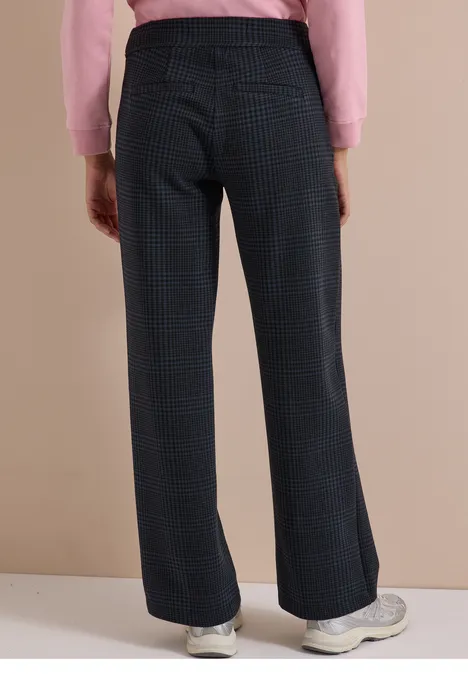 Iemand draagt een geruite, wijde broek met witte sneakers voor een beige achtergrond.
