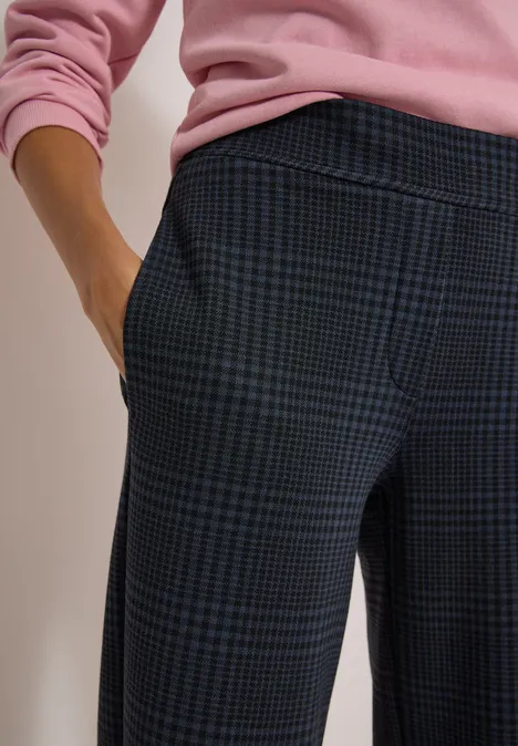 Close-up van een persoon in geruite broek en roze trui, hand in zak