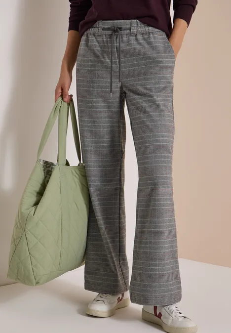 Grijze ruitbroek met wijdvallende pijpen, lichte gewatteerde groene tas en witte sneakers.