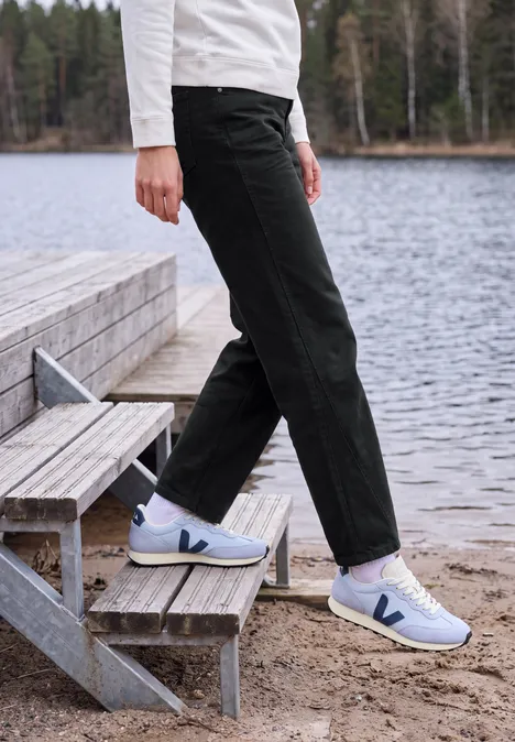 High Waist Barrel Leg Jeans im Loose Fit Black Person trägt schwarze Hose und weiße Sneaker auf hölzerner Treppe am Ufer eines Sees.