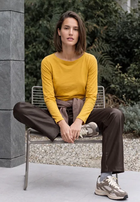 Broek met High Waist en Wide Leg pijpen in leerlook truffle brown Frau in gelbem Pullover und brauner Hose sitzt entspannt auf einem Outdoor-Stuhl