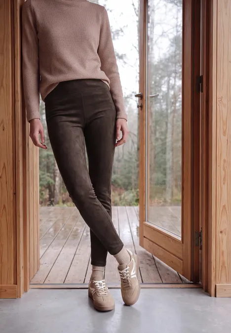 Personne debout dans une porte en bois, portant un pantalon en velours côtelé marron et des chaussons beiges.